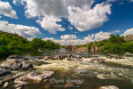 Fast river with rapids and rocky banks under picturesque clouds in sunny summer day