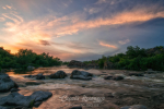 Fast river with rapids and rocky banks under picturesque sky at summer evening