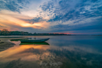 Lonely boat on the river at sunset. Picturesque clouds reflected in calm water
